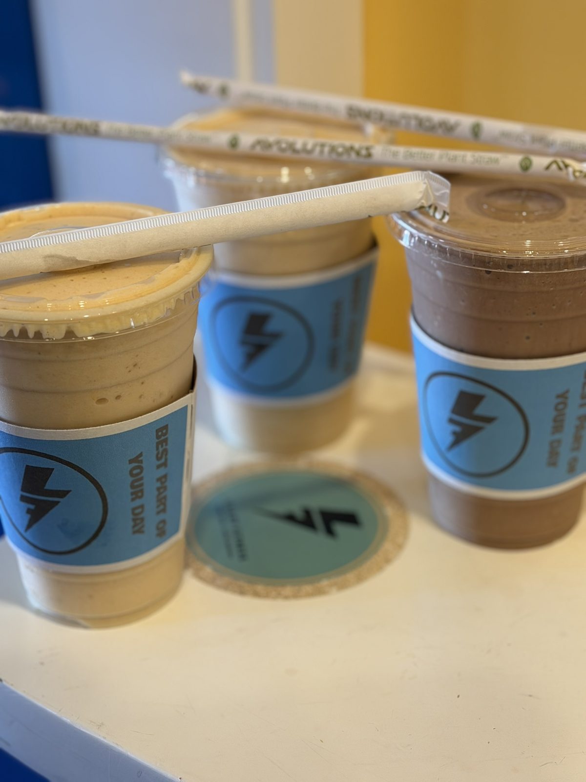 Three Lilley Fitness protein smoothies on the counter, in blue lightning-bolt sleeves that say Best part of your day.